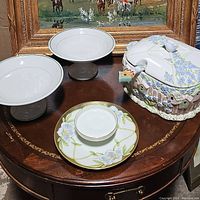 Photo shows two white pedestal dishes with green trim and gray bases, one floral serving plate with white and light green coloring, and a birdhouse-themed soup tureen with lid decorated with pastel blue flowers and 3D birdhouse details.
