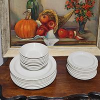 Stack of 8 bowls, 12 dessert plates, and 8 dinner plates displayed on wooden surface with painting behind