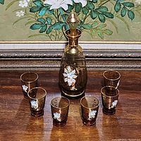 Front view of the decanter with six glasses arranged around it showing the complete set and floral designs