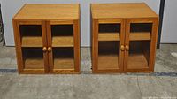 Pair of wood two-door glass front cabinets side by side on a concrete floor showing front and top view.