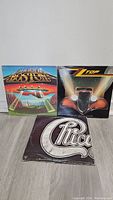 Three vinyl rock albums by Boston, ZZ Top, and Chicago displayed leaning on a wall.
