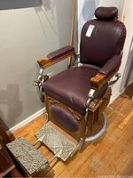 Front view showing burgundy leather seat and backrest, carved oak frame and metal pedestal base