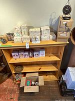 Photo of wooden shelving unit with multiple boxed Precious Moments figurines and boxed Christmas decor, some unboxed figurines displayed on top shelf, and cardboard box of assorted items beneath shelf.