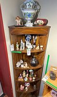 Full view of corner wooden shelf with various ceramic figurines and decorative items arranged on four shelves.