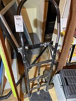 Front view of black metal hand truck showing frame and handle, with visible paint chips and missing one wheel.