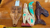 Three indigenous wood carvings on table: carved mask, painted bird figure, dark orca carving.