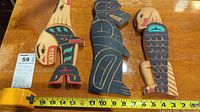Three carved wooden indigenous art figures on a wooden surface with measuring tape showing approximately 13 inches height