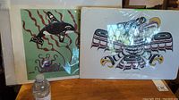 Image showing two indigenous art prints side by side on a wooden surface, one with a killer whale and the other with an eagle.