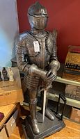 Full view of knight statue in armor on rectangular stand with folding dolly positioned behind