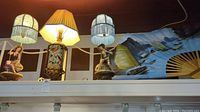 Three decorative lamps and large folding fan on display shelf