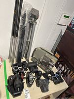 Overall view of two tripods, movie projector and assorted cameras and lenses on table
