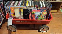 Red metal child's wagon filled with DVDs and CDs, showing the 'All Pro Express' label on the side and a variety of media cases inside.