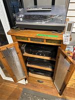 Full view of wooden cabinet with glass doors open showing turntable on top shelf and audio components inside