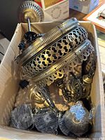 Photo of disassembled Turkish light fixture parts showing intricate brass-tone metal work and wiring inside a cardboard box