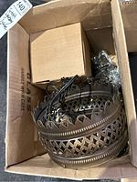 View of the main metal lamp decoration in a cardboard box showing lattice pattern and scalloped edges with attached wiring and chain.