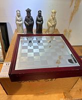 Large ceramic chess pieces shown standing atop original cardboard box; pieces are contrasting colors of cream and dark brown with detailed classical shapes.