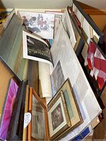 Stacked assortment of framed and unframed prints leaning against wall