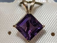 Close-up image of square-cut deep purple amethyst set in 10KT yellow gold pendant showing prong setting and bail