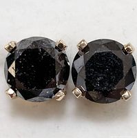 Frontal view of pair of round black diamond studs in four-prong gold settings on white background