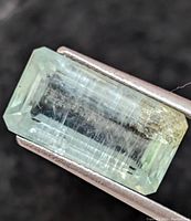 Close-up photos of a light blue-green emerald cut aquamarine gemstone held by tweezers showing internal inclusions and natural color variations.