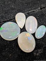 Five polished Australian opal gemstones with varying shapes including oval and pear. Display characteristic opal play-of-color on dark background.