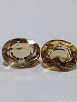 Front view of two oval faceted citrine gemstones showing their transparent golden-yellow color and cut facets.