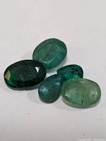Four genuine emerald gemstones with different cuts and shades of green laid on white background.