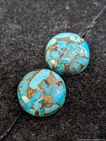 Two round turquoise cabochon gemstones with brown/golden matrix patterns on black background.
