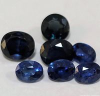 Seven oval-shaped faceted blue sapphire gemstones on white background, showing color and facets
