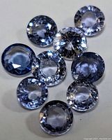 Close up view of nine loose round brilliant cut tanzanite gemstones showing their blue-violet color and facet details.