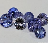 Seven loose tanzanite gemstones arranged on a flat surface showcasing their color and cut.