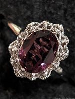 Close-up photo of the silver ring featuring an oval purple gemstone surrounded by clear stones on a black background.