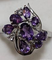 Close-up photo of the ring face showing multiple faceted amethyst stones and cubic zirconia accents set in sterling silver with swirling design.