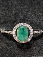 Close-up of emerald gemstone surrounded by small diamonds on sterling silver ring