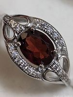 Close up of sterling silver ring with oval garnet and clear accent stones.