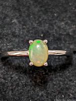 Close-up top view of sterling silver ring with oval opal gemstone showing the stone's color play and prong setting.