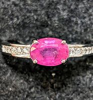 Top view of sterling silver ring with oval ruby and accent stones on band