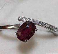 Close-up image of sterling silver ring featuring an oval-shaped ruby and a row of small clear stones on a curved band.
