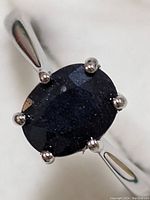 Close-up photo of the oval-shaped dark blue sapphire stone set in six prongs on a sterling silver band.