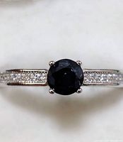 Front view of ring showing round dark blue sapphire center stone and clear accent stones on sterling silver band.