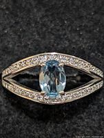 Top view of sterling silver ring with oval blue topaz center and clear accent stones on an open marquise-shaped band.