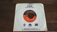 Photo of first 45rpm vinyl single showing the orange and black Atlantic label with Warner-Elektra-Atlantic logos and WEA paper sleeve from Canada.