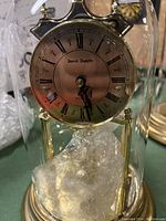 Close-up of Daniel Dakota glass dome mantel clock face with roman numerals and quartz movement, inside glass dome with brass finish