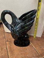 Photo showing the swan-shaped ceramic pitcher with dark marbled glaze next to tape measure showing height around 10-11 inches