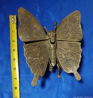 Top view of metal butterfly ashtray with tape measure showing approx 8 inches width