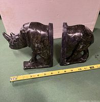 Side view of two carved stone rhino bookends placed side by side with measuring tape showing about 6 inches height.