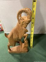 Photo showing carved wooden mountain ram sculpture with a measuring tape indicating height around 10 inches.