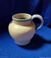 Side view of white ceramic water pitcher with blue handle and rim in blue trim