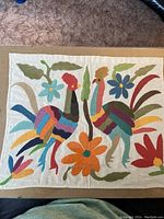 Photo of a vintage rectangular hand embroidered textile featuring two colorful birds and flowers in Otomi Tenango style.