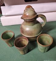 Green Frankoma pottery juice pitcher with lid and handle alongside three matching green pottery glasses with brown rim.